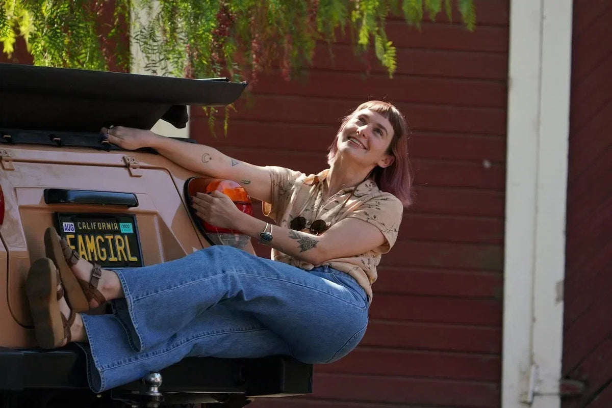 Woman wearing Famolare retro platform sandals with wide-leg jeans while sitting on the bed of a vintage pickup truck in a rustic outdoor setting.