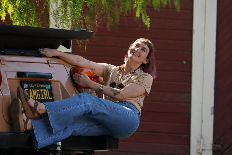 Woman wearing Famolare retro platform sandals with wide-leg jeans while sitting on the bed of a vintage pickup truck in a rustic outdoor setting.
