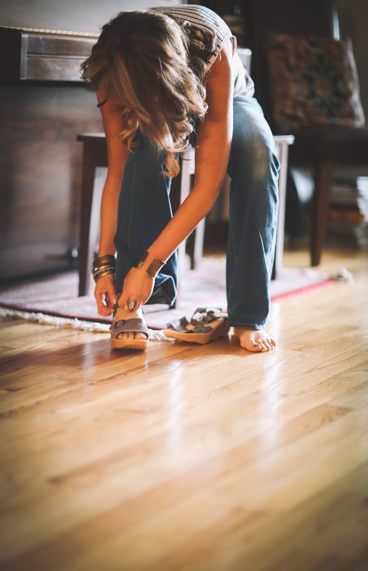 Woman adjusting neutral Famolare sandals while wearing blue jeans and a relaxed white summer top.