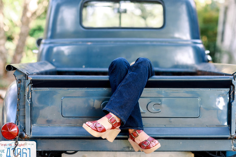 Woman wearing red Famolare platform sandals with blue jeans while sitting on the back of a vintage pickup truck.